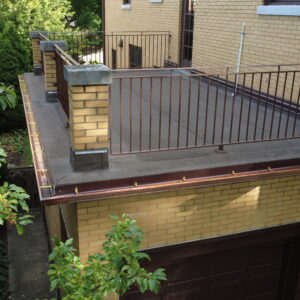 Flat roof deck over garage with new metal railings, fresh roofing surface, and copper gutters on a yellow brick home.