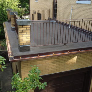 Flat roof deck above garage with metal railings, new roofing surface, and copper gutters on a yellow brick home.
