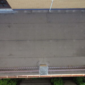 Aerial top-down view of a flat roof deck with new roofing membrane, metal railings, and updated edge flashing on a brick home.