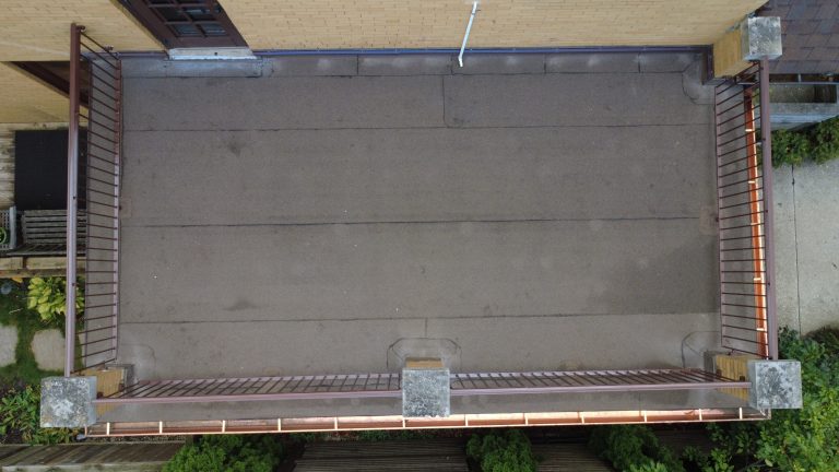 Aerial top-down view of a flat roof deck with new roofing membrane, metal railings, and updated edge flashing on a brick home.