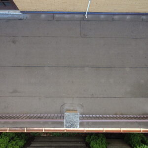 Top-down aerial view of a flat roof deck with a clean roofing membrane, metal railings, and updated flashing on a brick home.