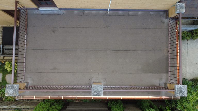 Top-down aerial view of a flat roof deck with a clean roofing membrane, metal railings, and updated flashing on a brick home.