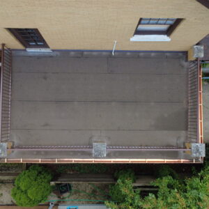 Aerial view of a flat roof deck with clean roofing membrane, metal railings, and new copper gutters on a brick home.