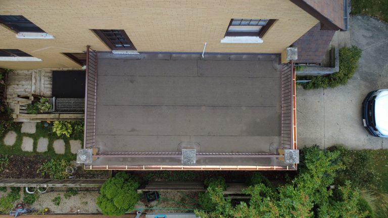 Aerial view of a flat roof deck with clean roofing membrane, metal railings, and new copper gutters on a brick home.