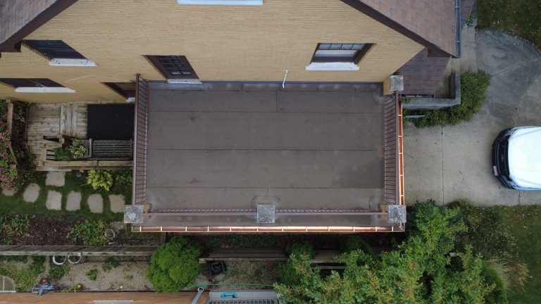 Aerial view of flat roof deck on brick home with smooth roofing membrane, updated railings, and new copper gutters.