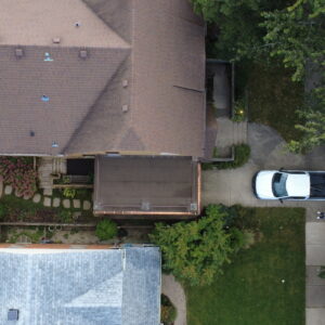 Aerial overhead view of a brick home with a restored flat roof deck, surrounding landscaping, patio area, and driveway.