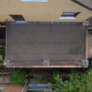 Aerial view of a restored flat roof deck on a brick home with clean roofing membrane, updated railings, and copper gutters.