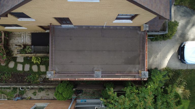Aerial view of a restored flat roof deck on a brick home with clean roofing membrane, updated railings, and copper gutters.