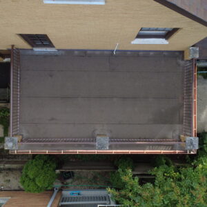 Aerial top-down view of a restored flat roof deck on a brick home with clean roofing membrane, metal railings, and copper gutters.
