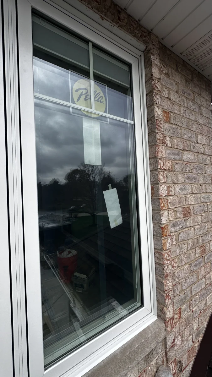 Close-up of a newly installed white-trim Pella window on a brick home exterior.