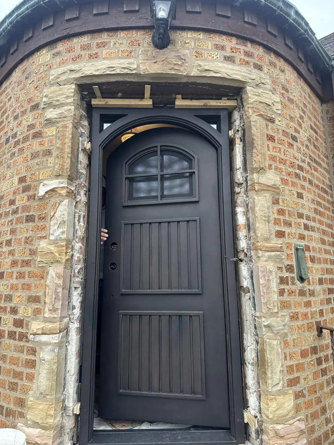 New arched iron entry door with speakeasy grille installed in a brick turret entryway