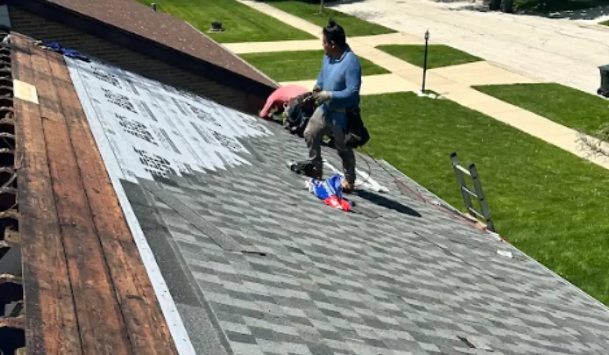 Two professional roofers installing asphalt shingles on a suburban Illinois home during warm weather.