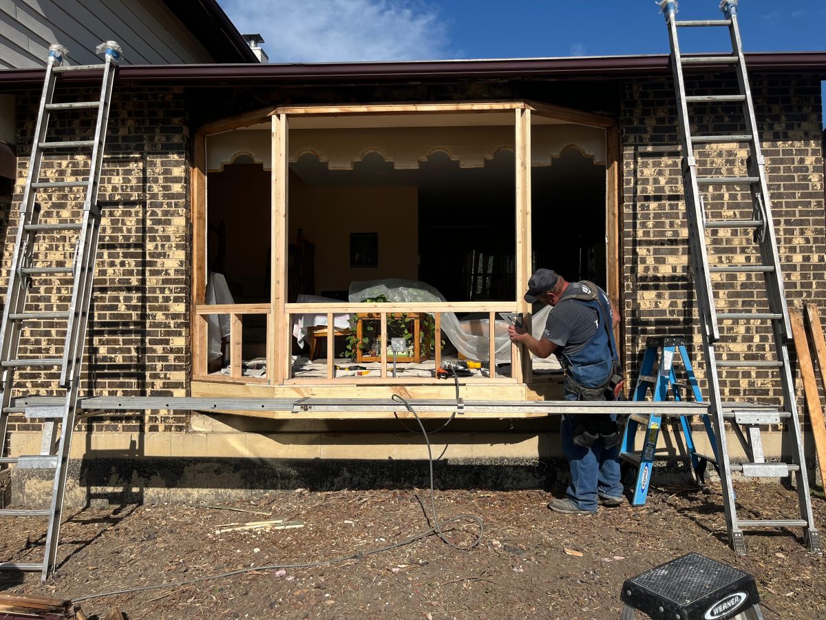 Crew rebuilding the frame for a replacement bay window on a brick home