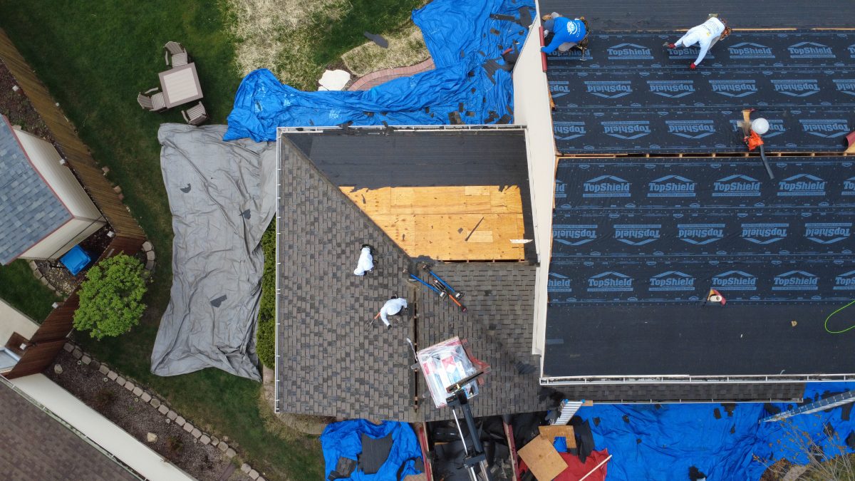 Aerial view of roofing contractors installing new shingles and underlayment during a roof replacement project.