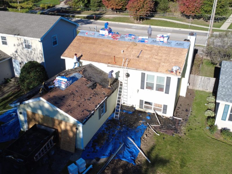 Aerial view of a residential home getting a roof replacement by roofing contractors during the tear-off phase, showing old shingles removed and new underlayment being installed.