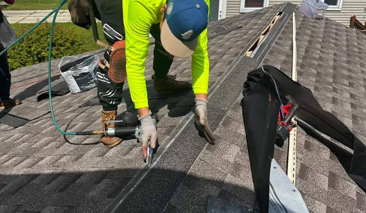 Roofing companies install asphalt shingles as a contractor measures and aligns materials precisely on a residential rooftop.