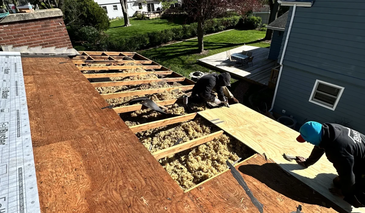 Roofing contractors replace plywood sheathing after severe storm damage, exposing insulation and structural roof framing.