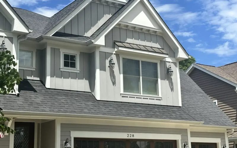 Craftsman-style two-story home with gray board-and-batten siding, dark asphalt shingle roof, and wood carriage-style garage doors