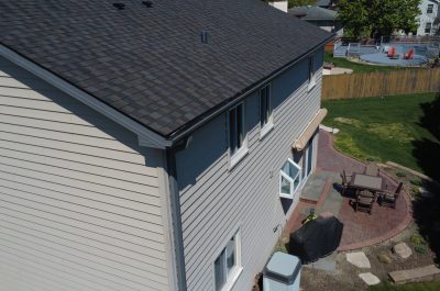 Close-up view of a newly installed dark gray asphalt shingle roof with fresh black gutter system on a two-story home.