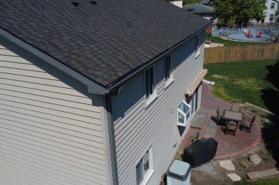 Close-up view of a newly installed dark gray asphalt shingle roof with fresh black gutter system on a two-story home.
