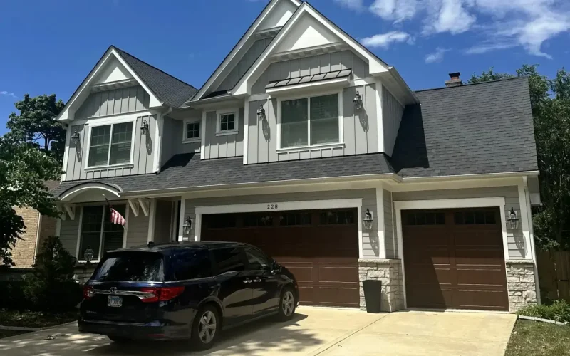 Two-story white board-and-batten farmhouse with dark asphalt shingle roof and three-car garage