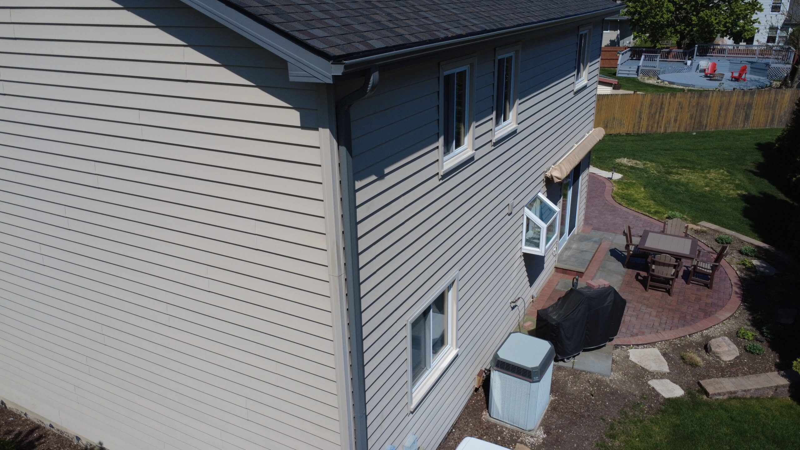 Side view of a two-story home with new dark gray asphalt shingles and freshly installed gutters above a backyard patio.