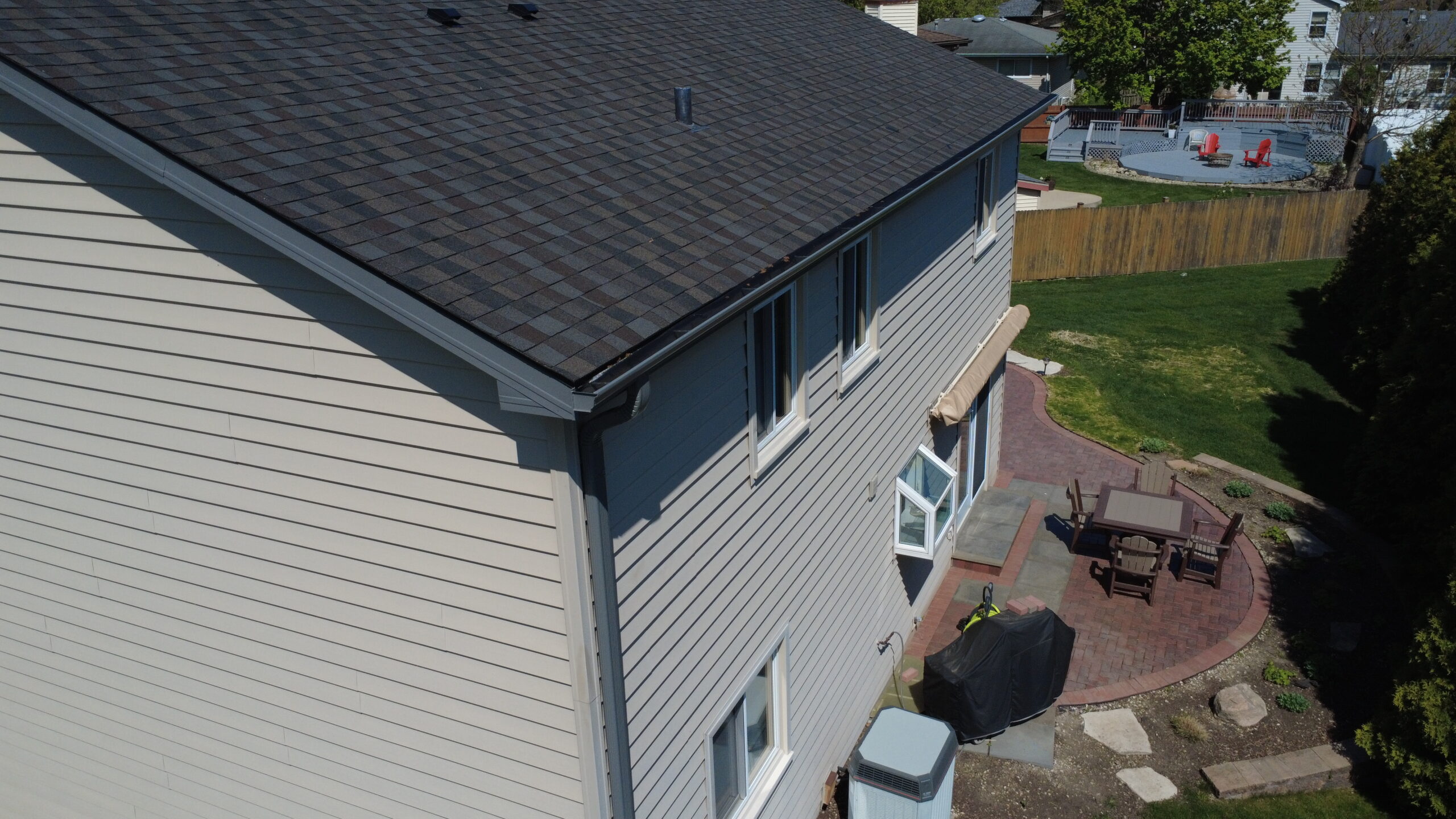 Close-up view of a newly installed dark gray asphalt shingle roof with fresh black gutter system on a two-story home.
