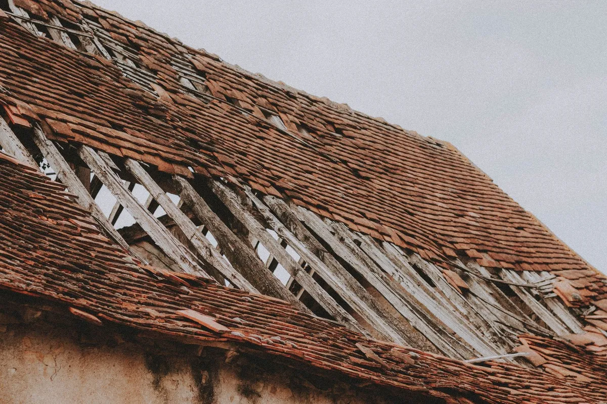 Close-up of an old roof with missing shingles and exposed wooden beams, highlighting potential inspection oversights.