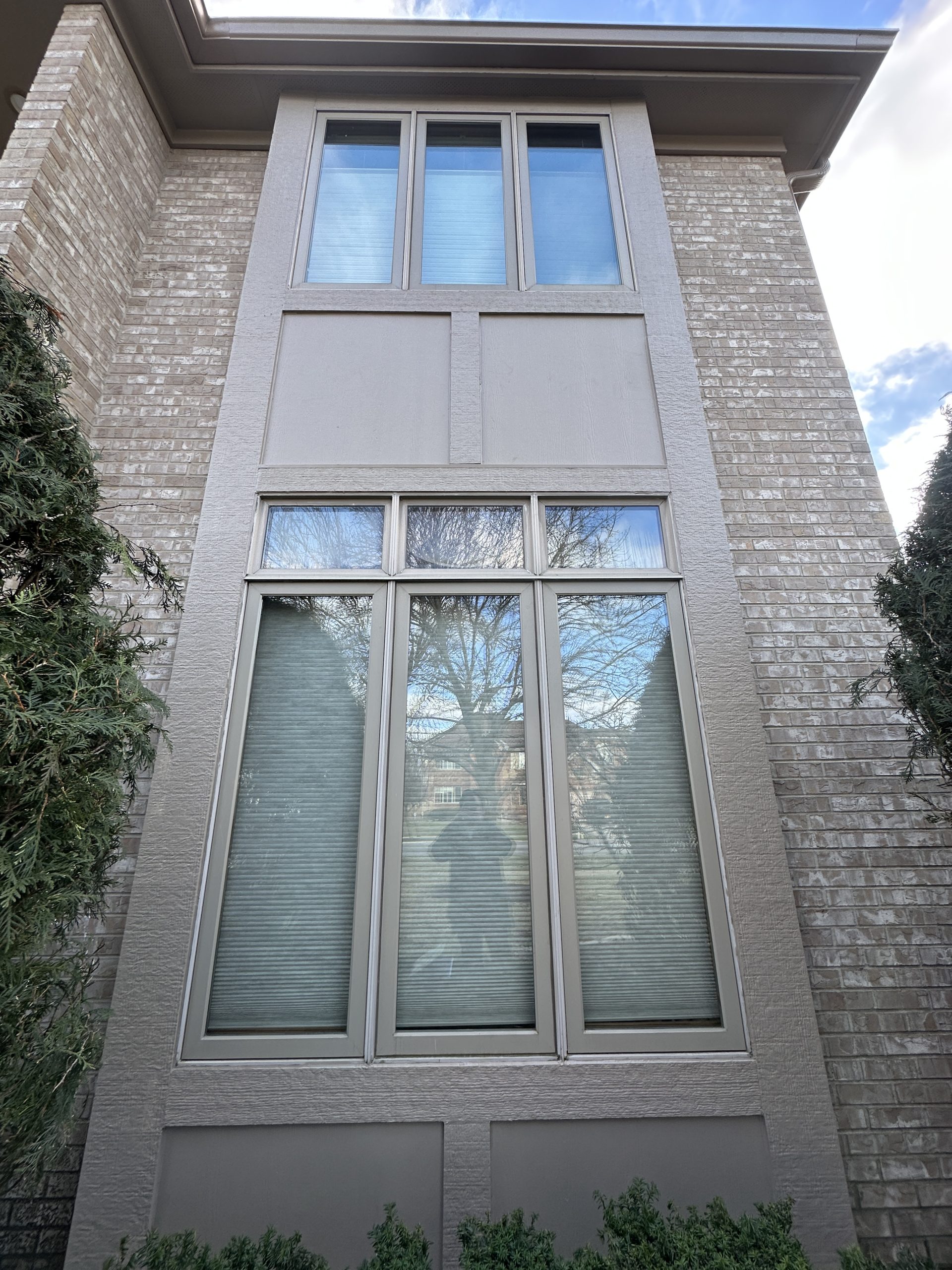 Tall stacked replacement windows with taupe frames on a modern brick and stucco home