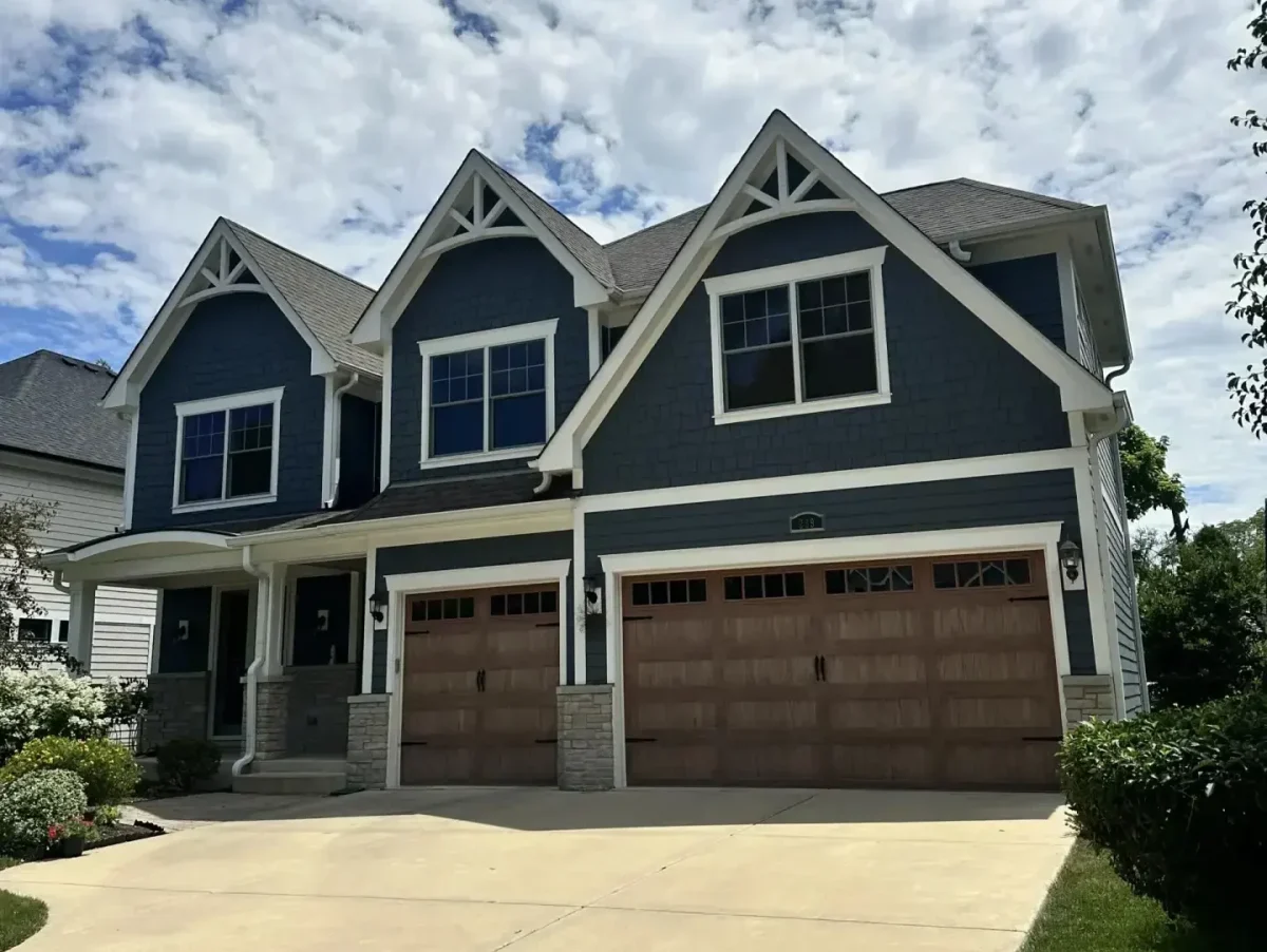 Two-story craftsman home with navy blue shake siding, twin white peaked gables, and wood garage doors