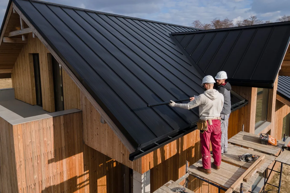 Roofers in helmets collaborating on a roof, highlighting teamwork in preventing costly repairs.