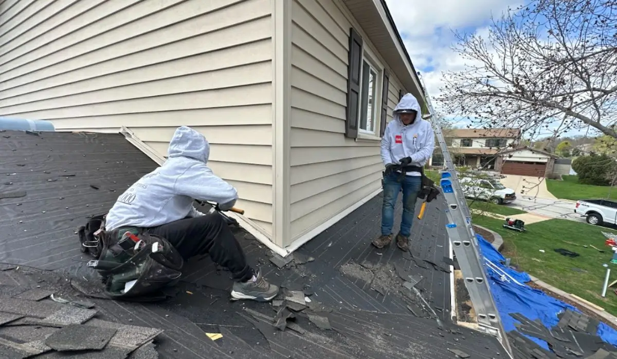 Two professional roofers removing damaged shingles during an emergency roof repair to restore home safety.