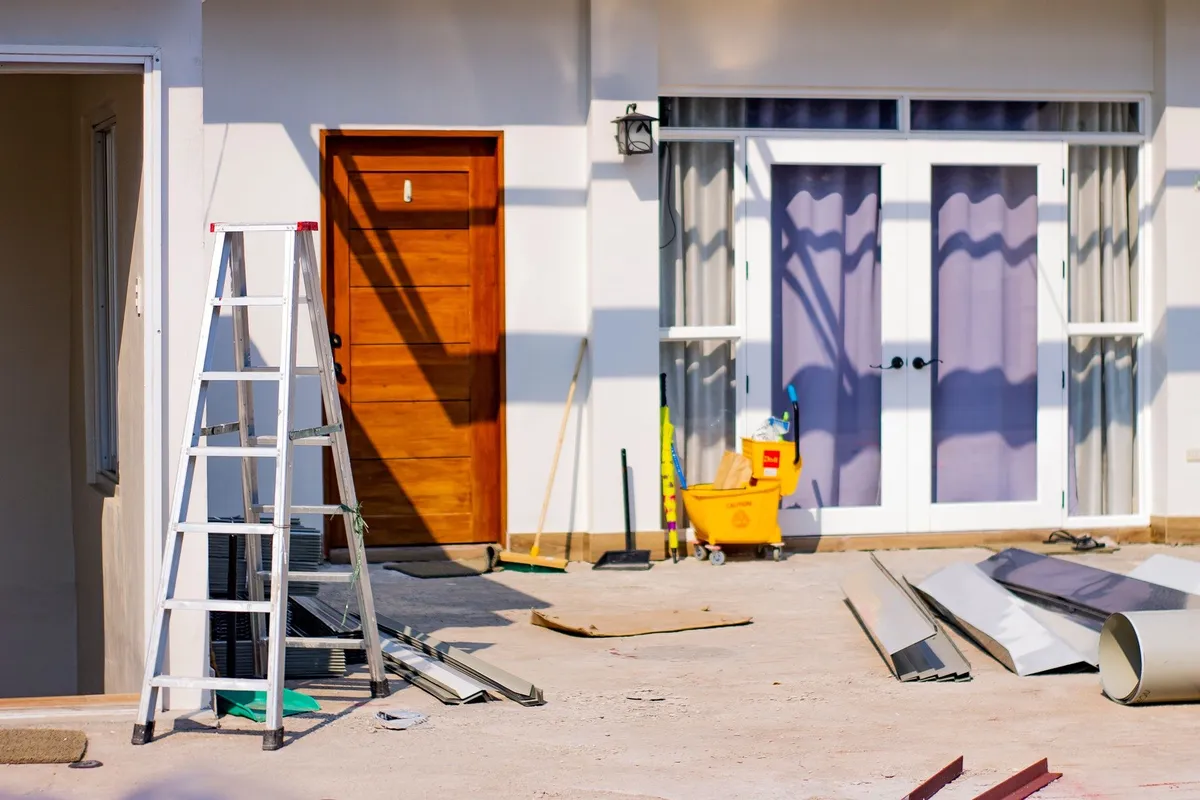 Front entrance of a house under renovation with tools and materials, highlighting the siding installation process.