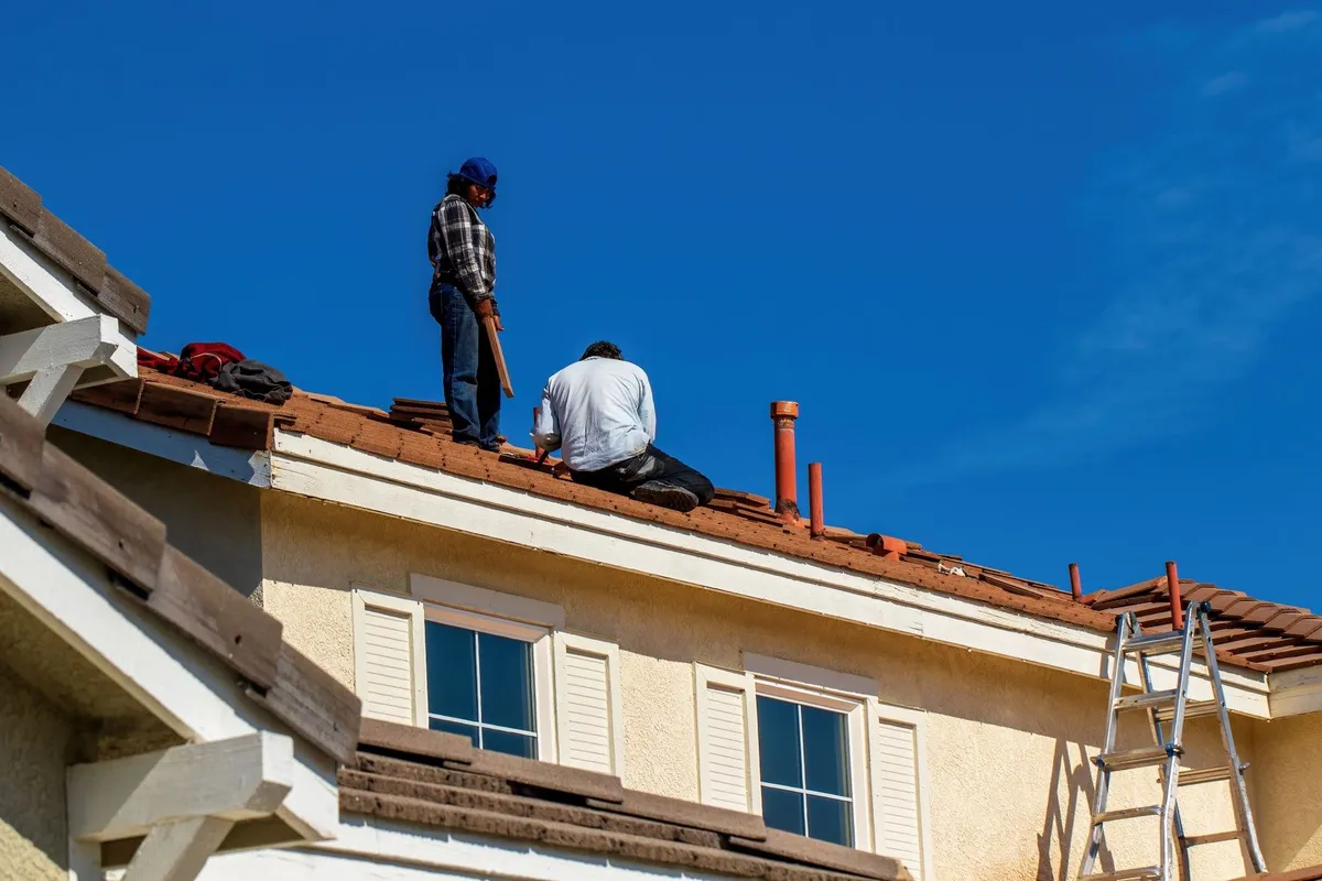 Workers installing tiles on a roof under a clear blue sky, relevant to hiring a roofing company.