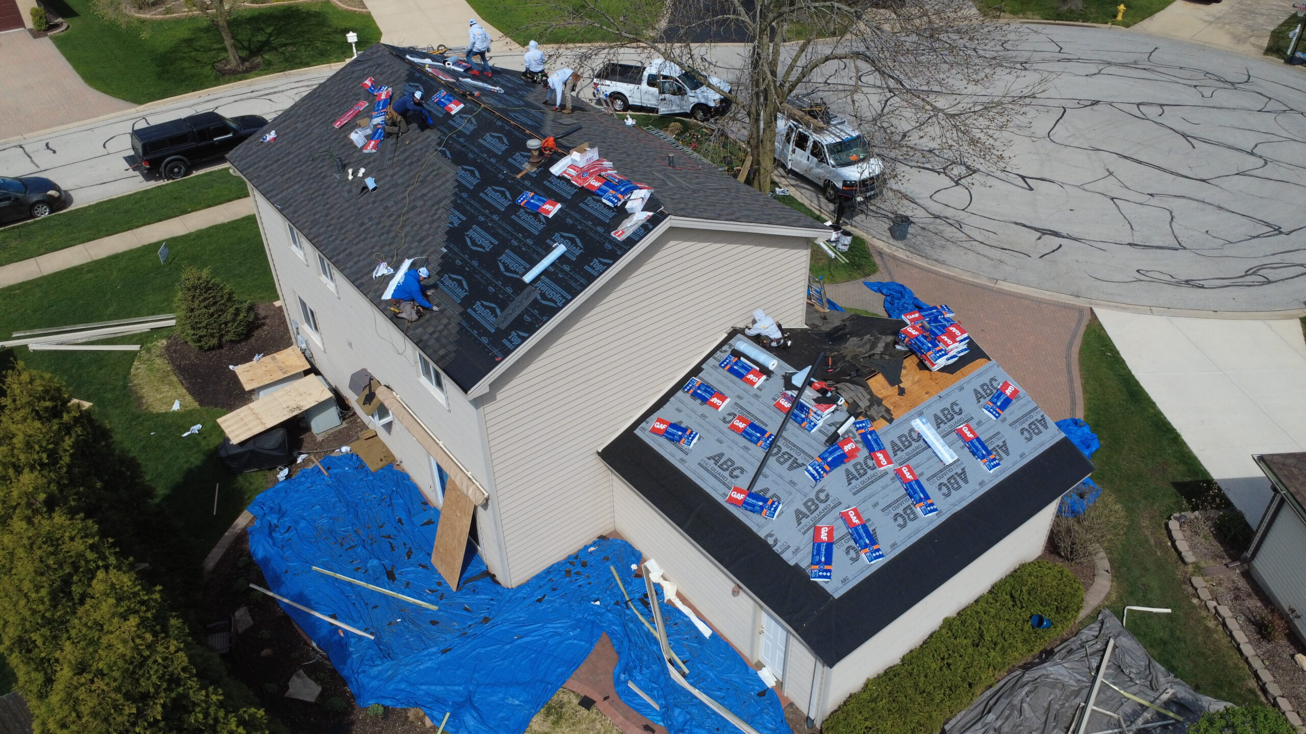 Aerial view of roofing contractors installing new shingles and underlayment on a two-story home during a roof replacement.