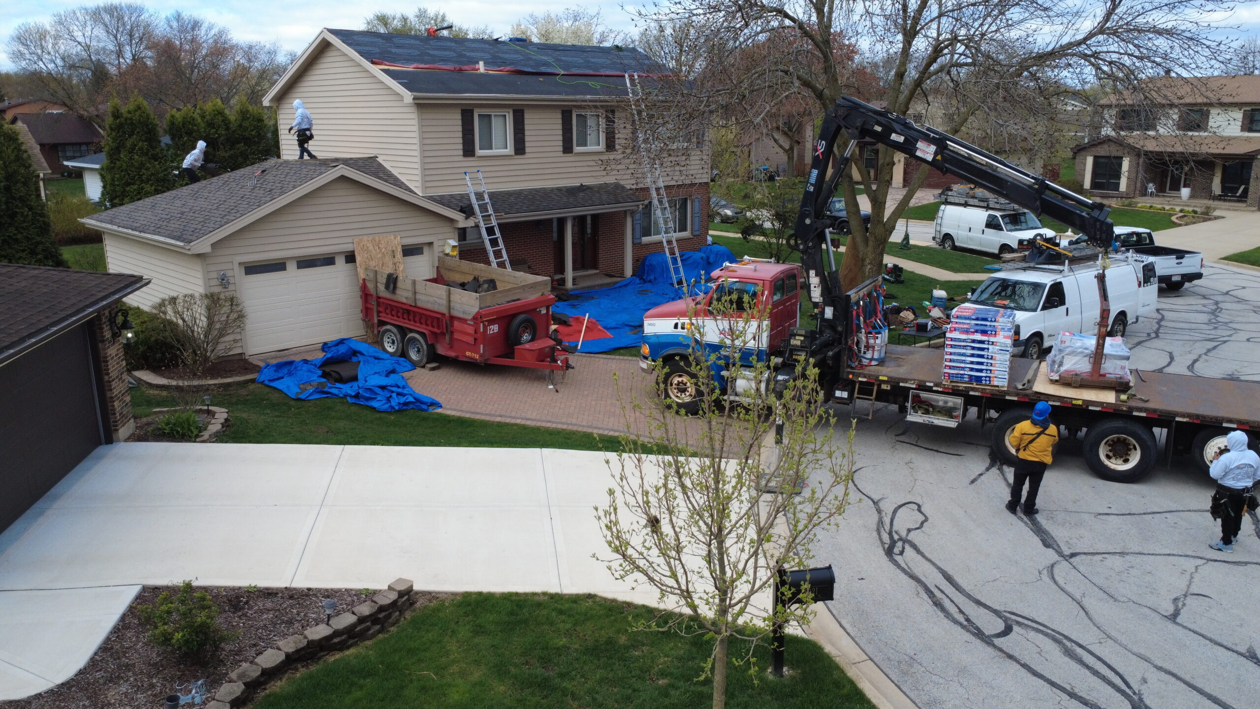 Roofing crew preparing a two-story home for roof replacement with underlayment, ladders, and material delivery trucks.