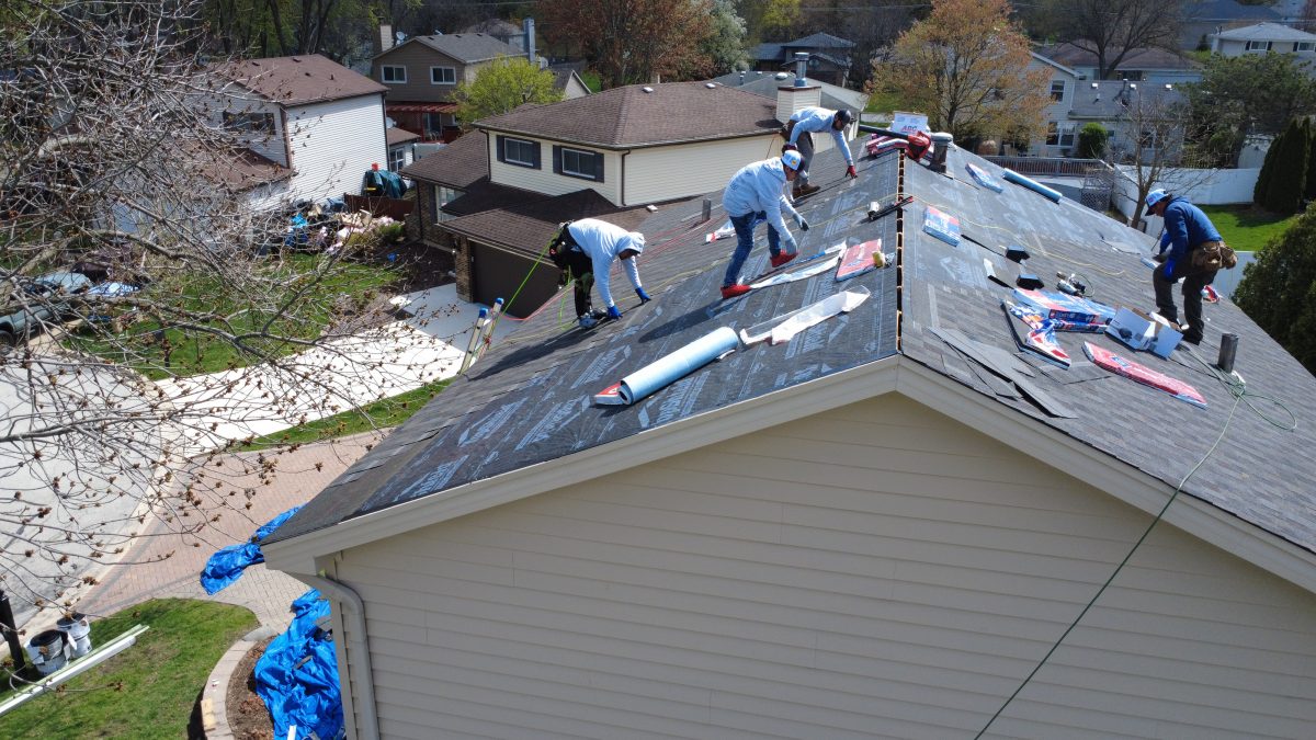Roofing contractors installing underlayment and preparing shingles on a residential roof during replacement.
