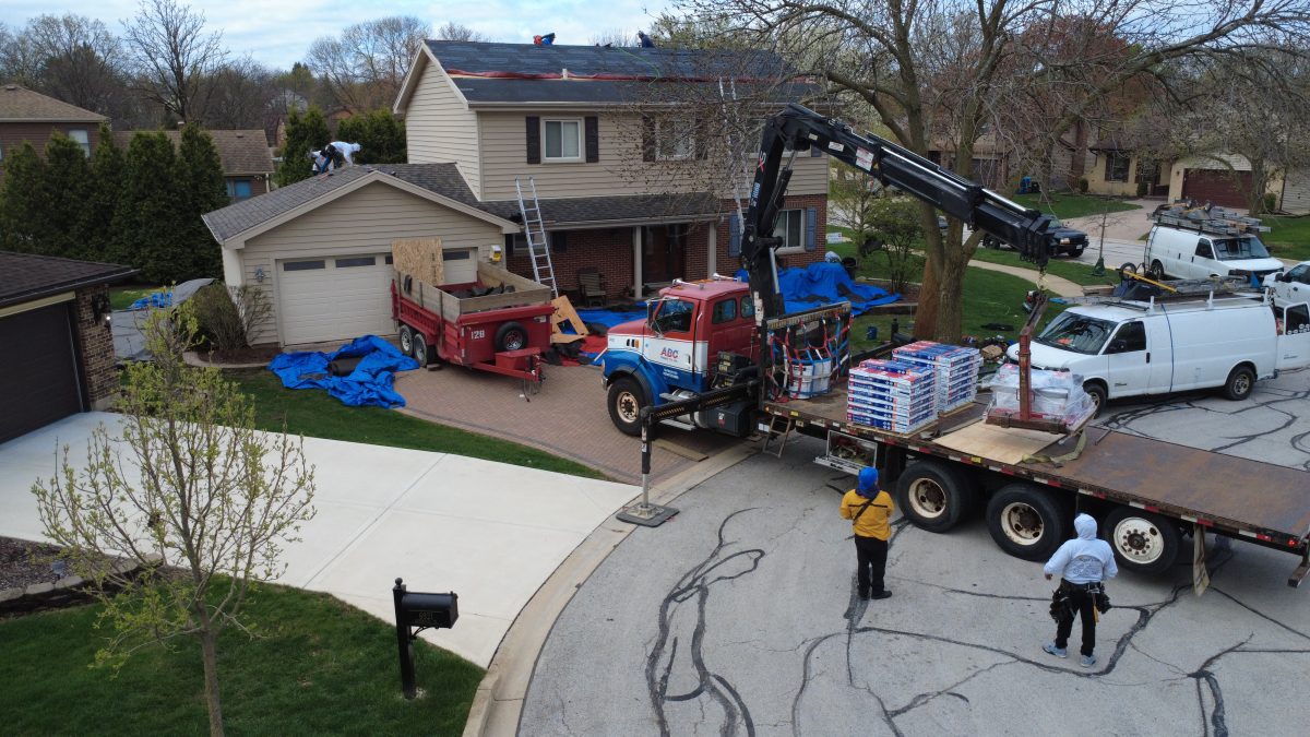 Roofing contractors preparing a two-story home for roof replacement with underlayment, material delivery, and equipment onsite.