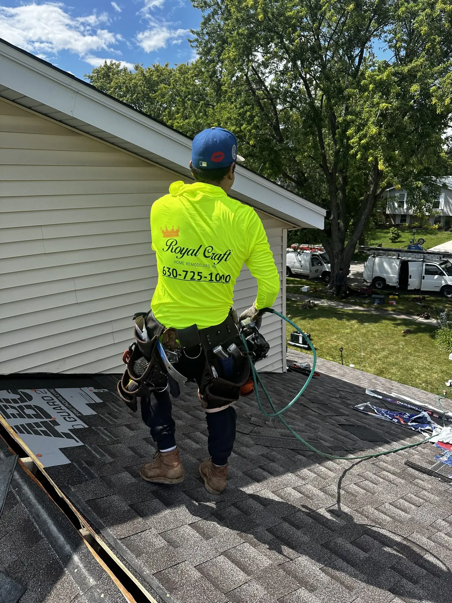 Royal Craft roofer in hi vis gear working on a rooftop with company vans parked below