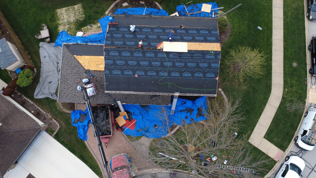 Overhead view of roofing contractors installing underlayment and repairing decking during a residential roof replacement.