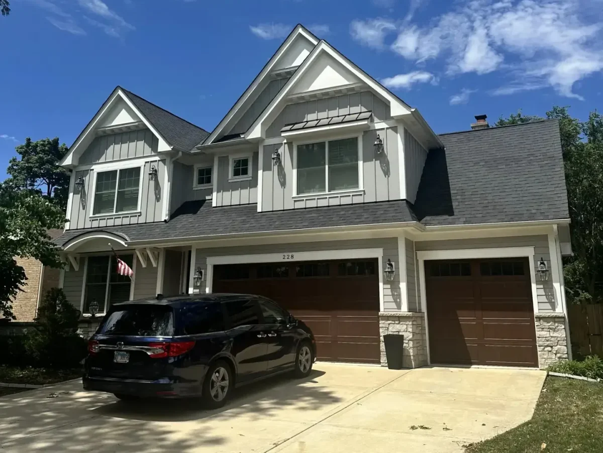 Two-story white board-and-batten farmhouse with dark asphalt shingle roof and three-car garage