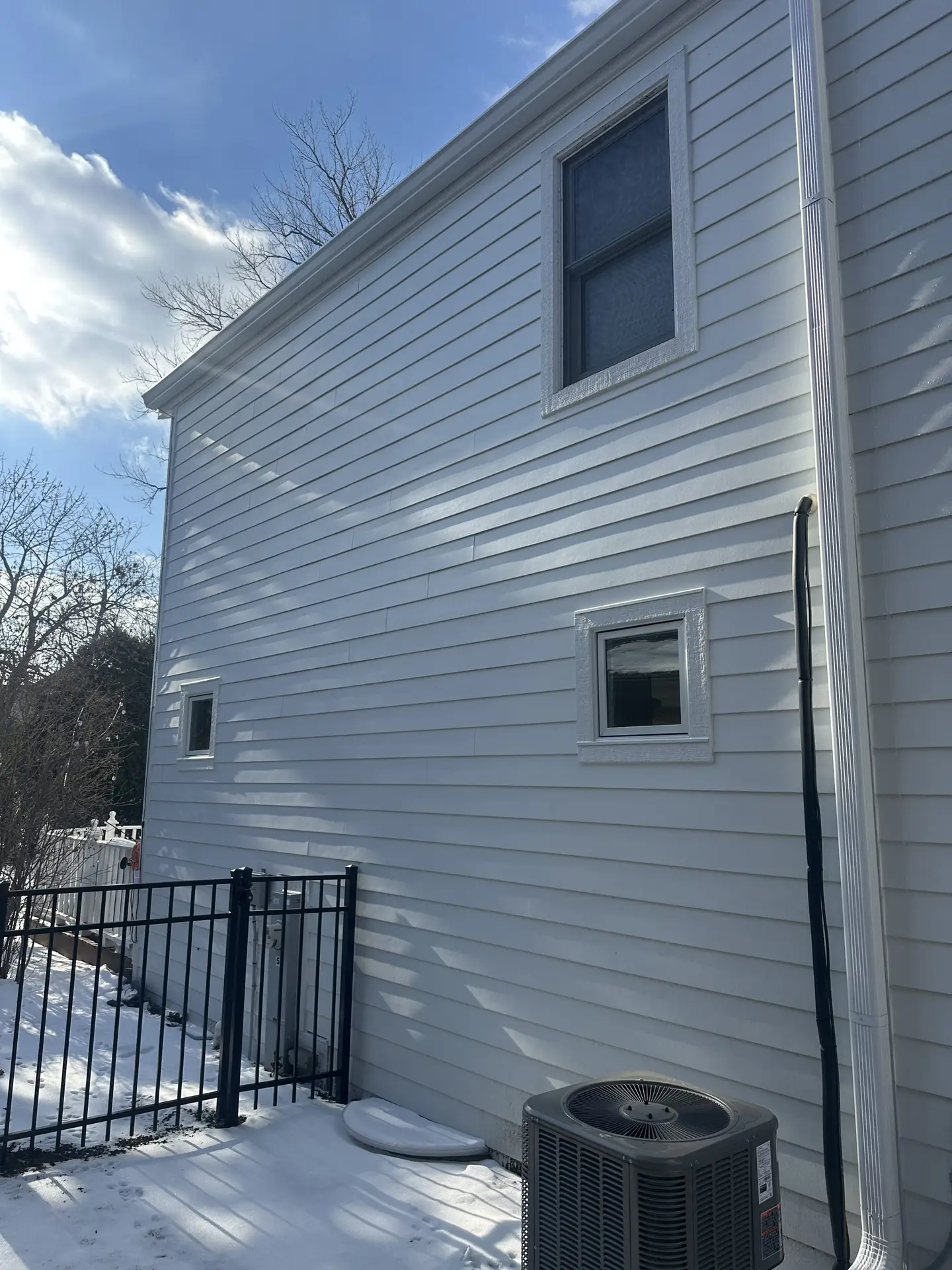Side elevation of a two-story home with new white vinyl siding and replacement windows
