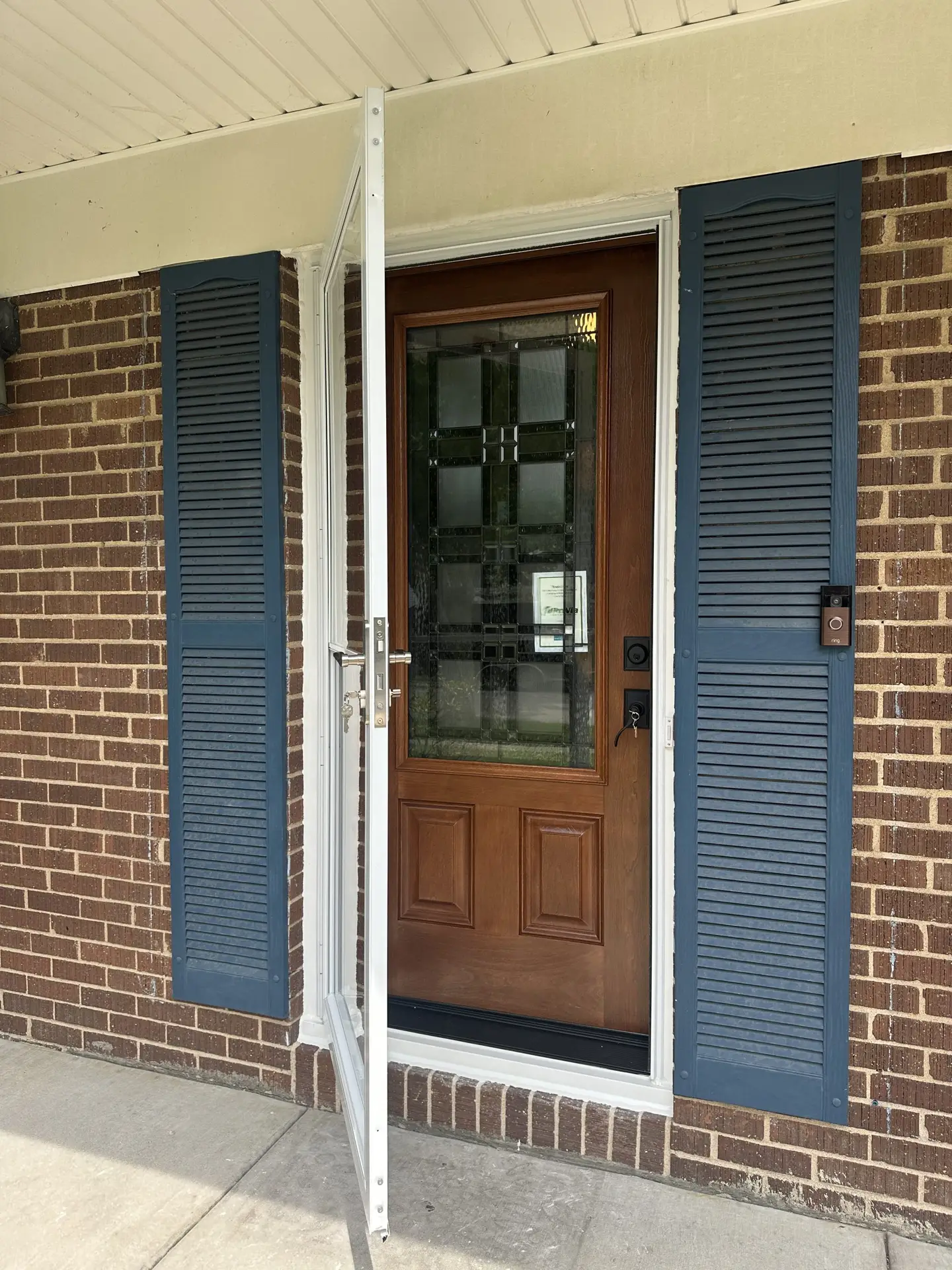 Wood-look entry door with decorative stained glass behind an open storm door